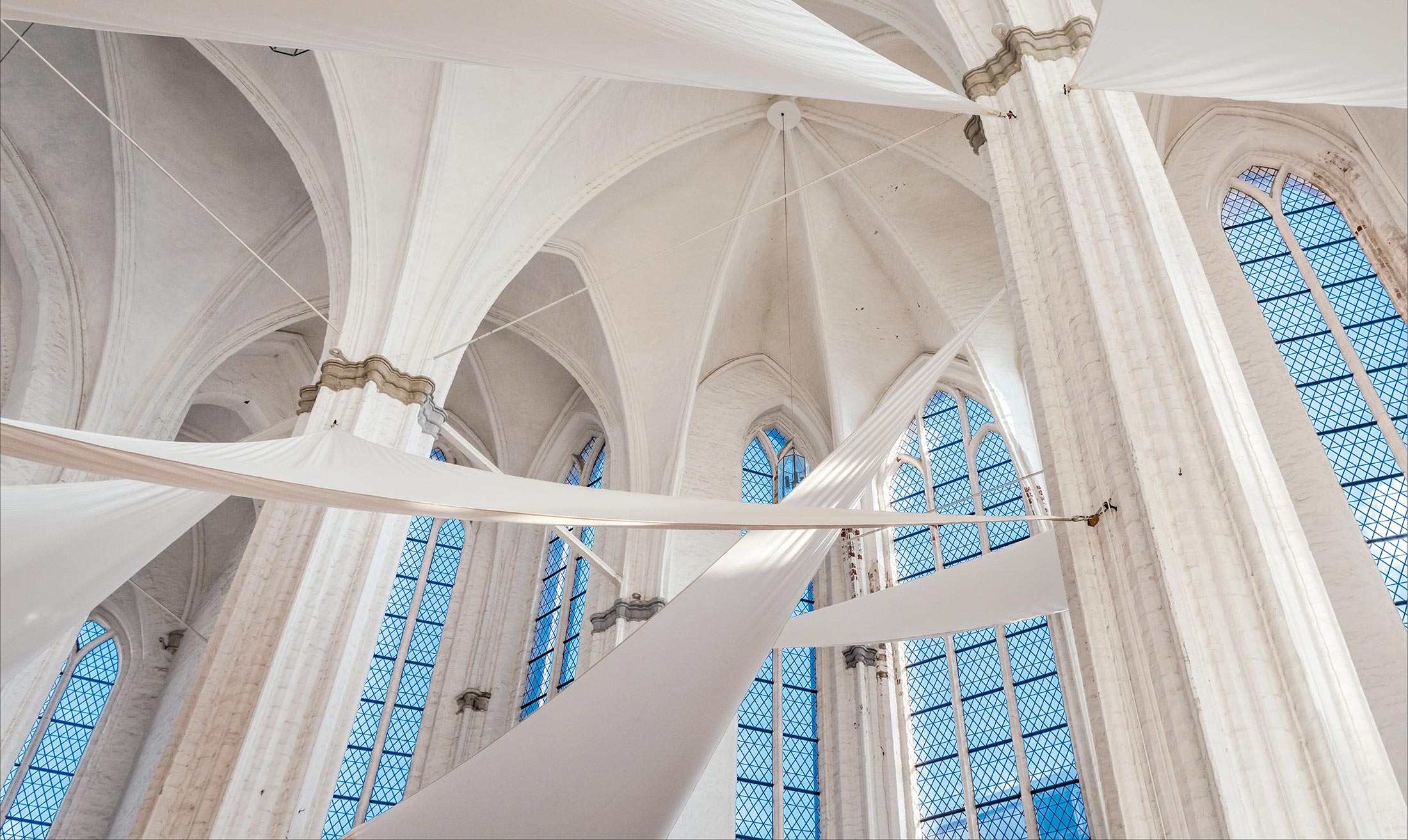 Blick nach oben in das Kirchenschiff der St. Petri-Kirche in Lübeck. Im Vordergrund zwischen Säulen verspannte Sonnensegel.